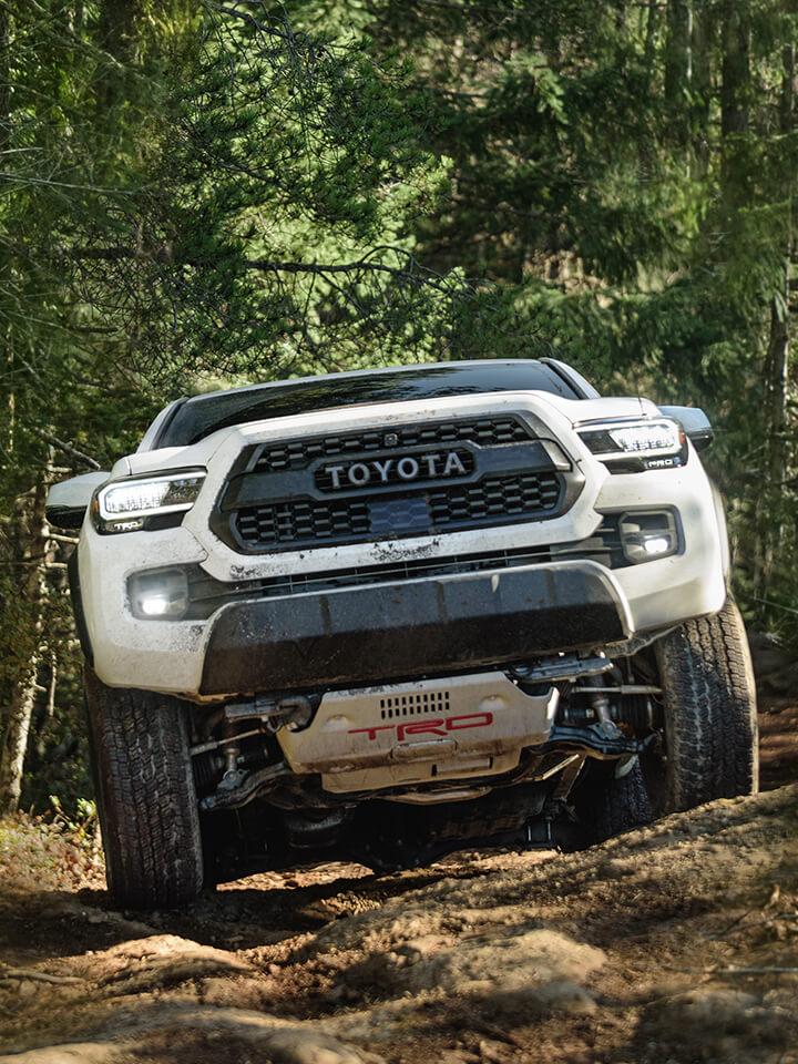 White Toyota Tacoma front angle shot driving on a rocky mountain path