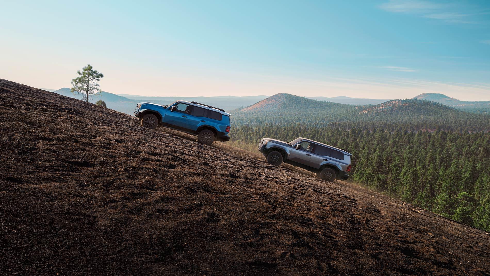 blue 2025 Toyota Land Cruiser hybrid climbing a mountain hill followed by an older generation Land Cruiser