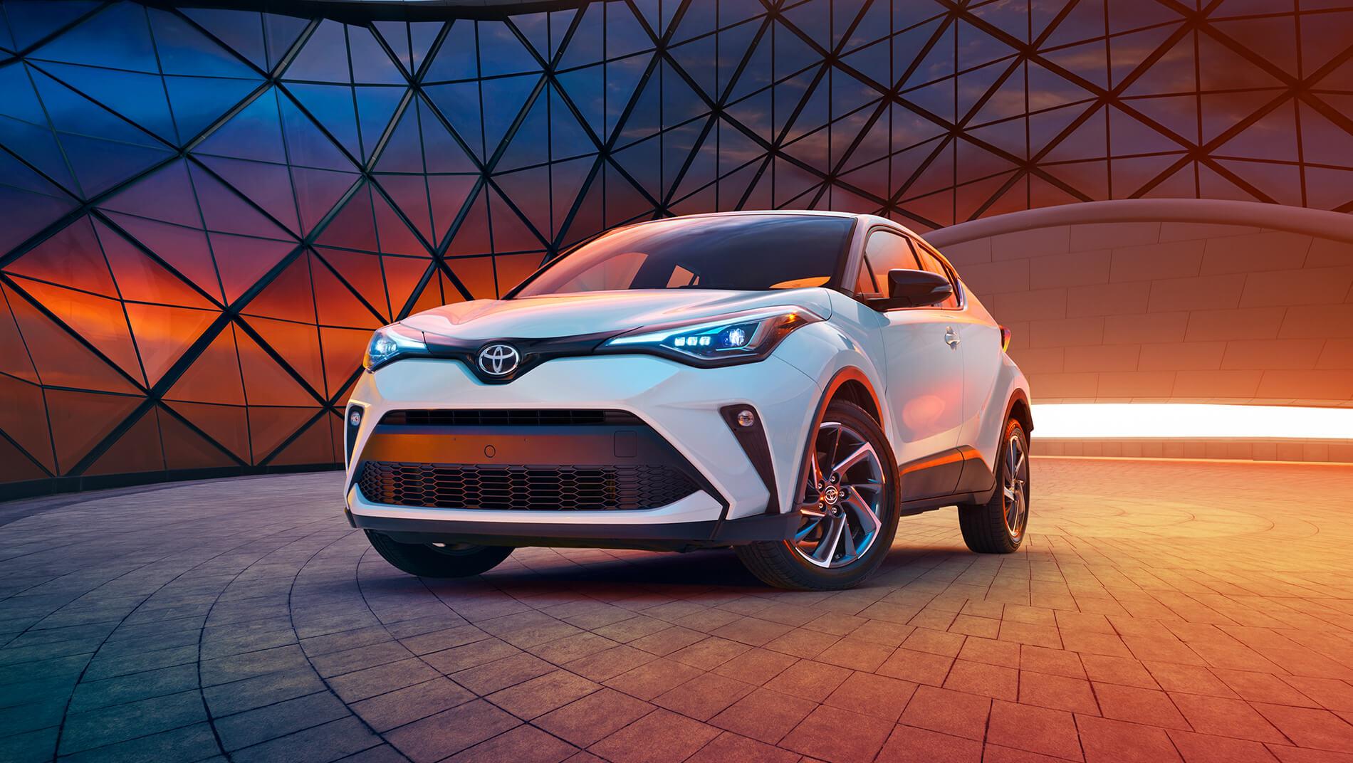 white Toyota C-HR parked in front of a glass building at sunrise