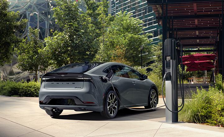 exterior image of a Grey 2024 Toyota Prius Prime plug in hybrid plugged into a charging station in the middle of the city