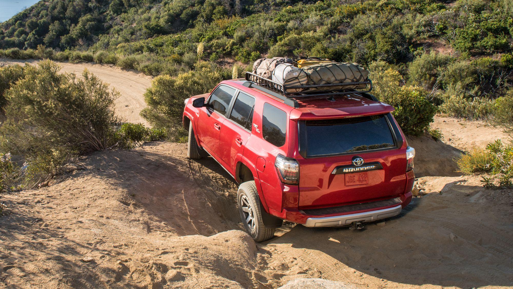 Red 2024 Toyota 4Runner with roof rack loaded with gear driving off road on a mountain