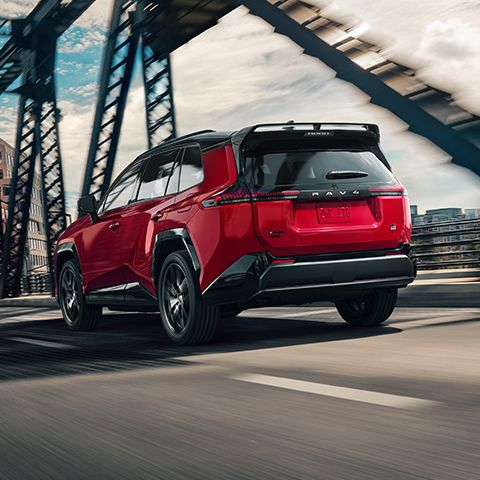 A Toyota RAV4 drives across a bridge in an urban setting, viewed from the rear.