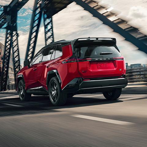 A Toyota RAV4 drives across a bridge in an urban setting, viewed from the rear.