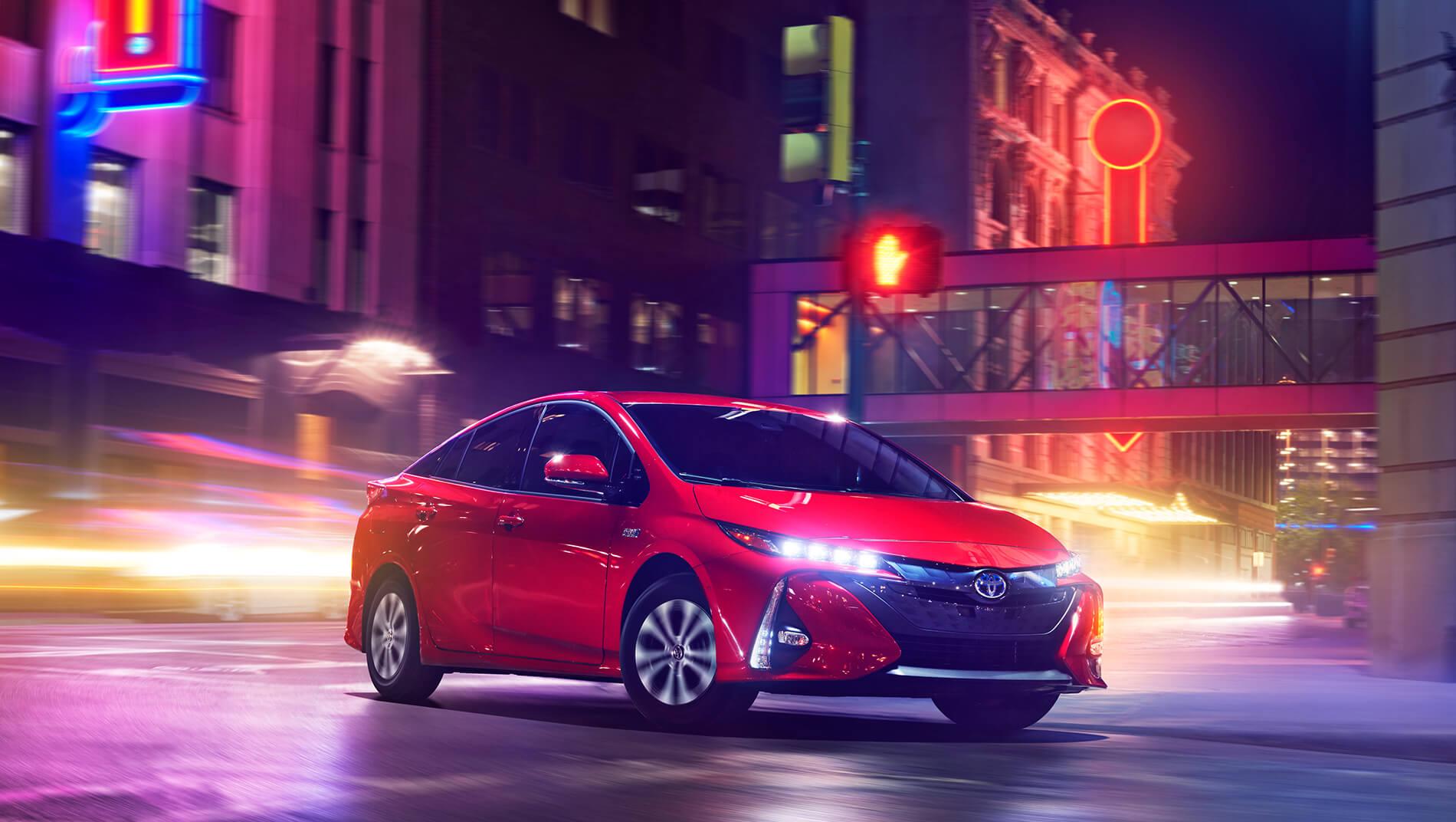 red Toyota Prius Prime plug in hybrid driving down city street at night