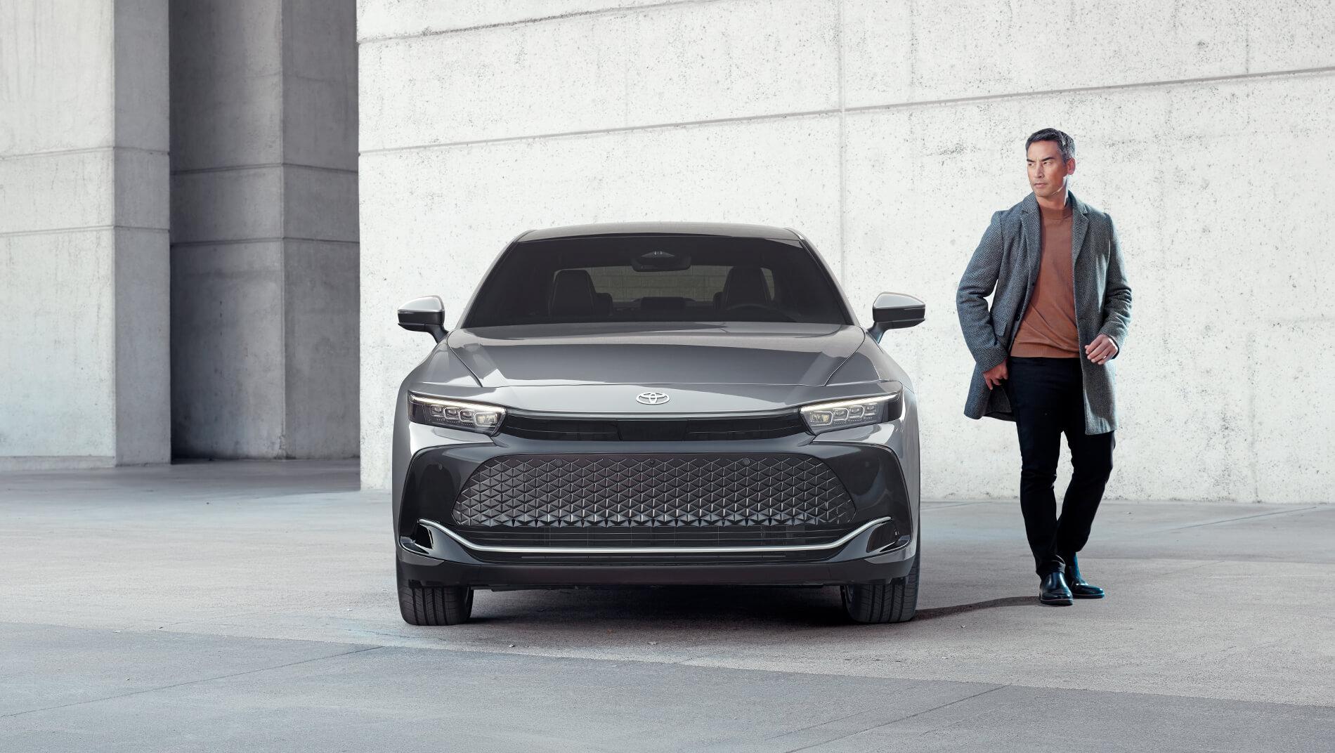 Man standing next to a silver Toyota 2023 Crown that is parked in front of a concrete building