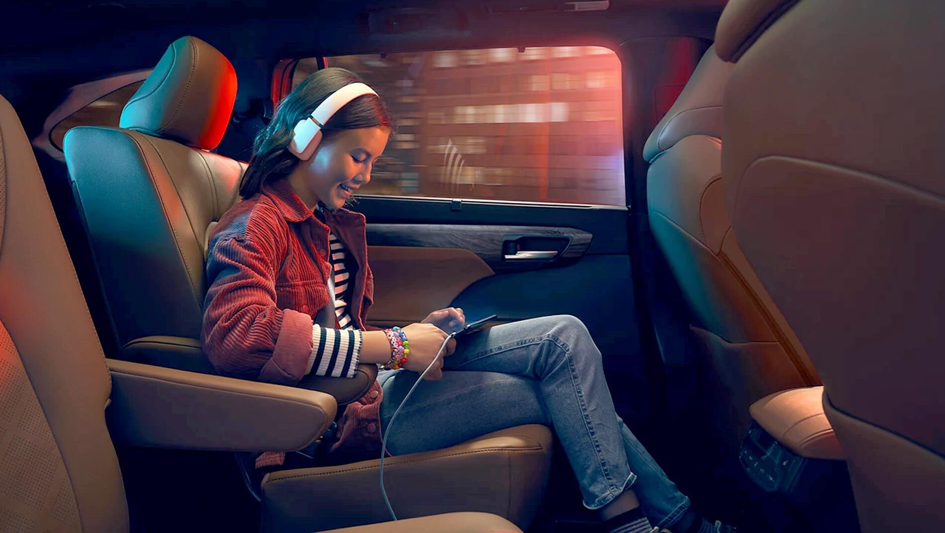girl sitting in back seat of a Toyota Highlander using her phone while charging it
