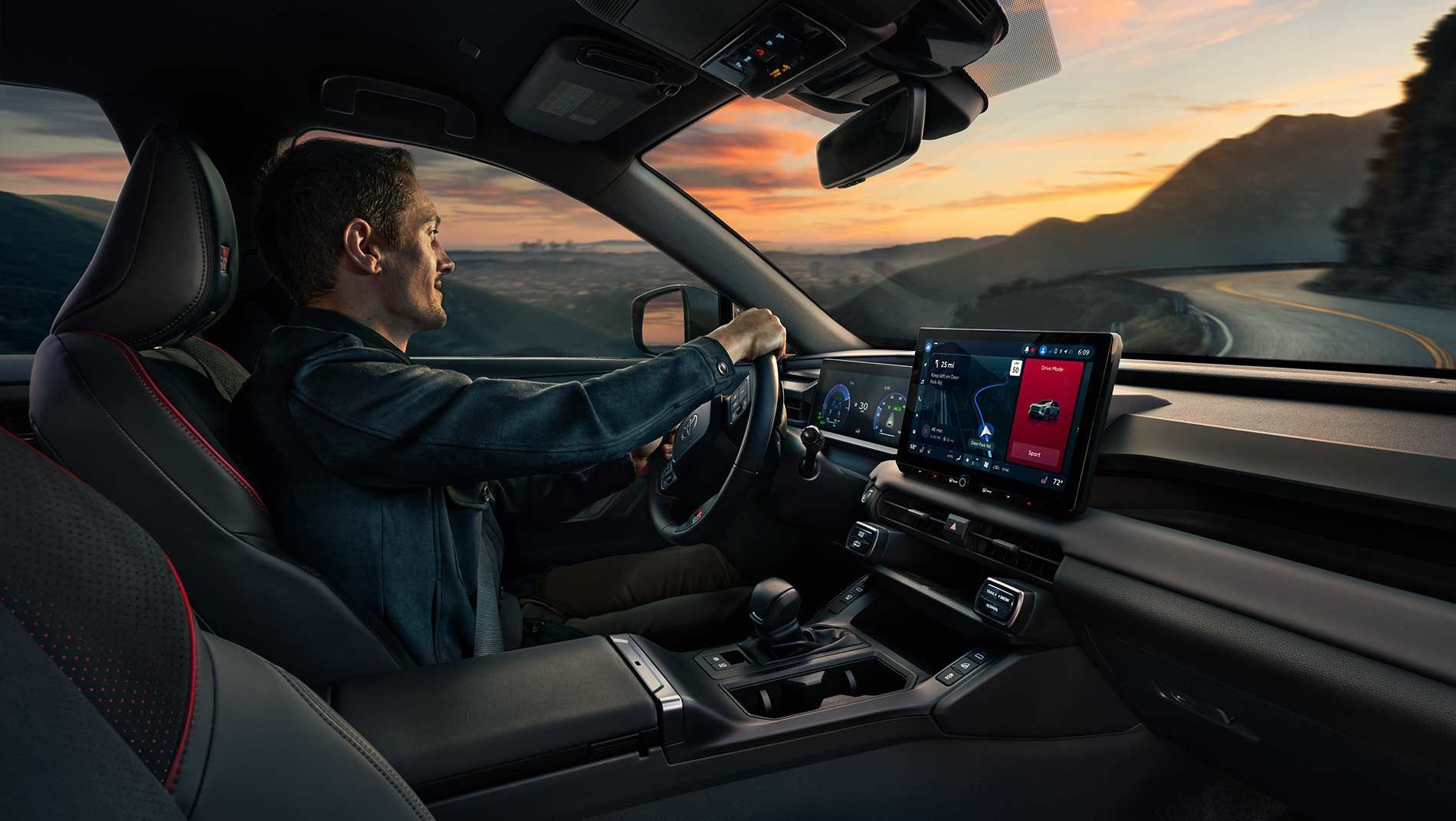 A man drives a RAV4 Plugin SUV on a winding mountain road at sunset, with the car's digital dashboard and infotainment screens glowing