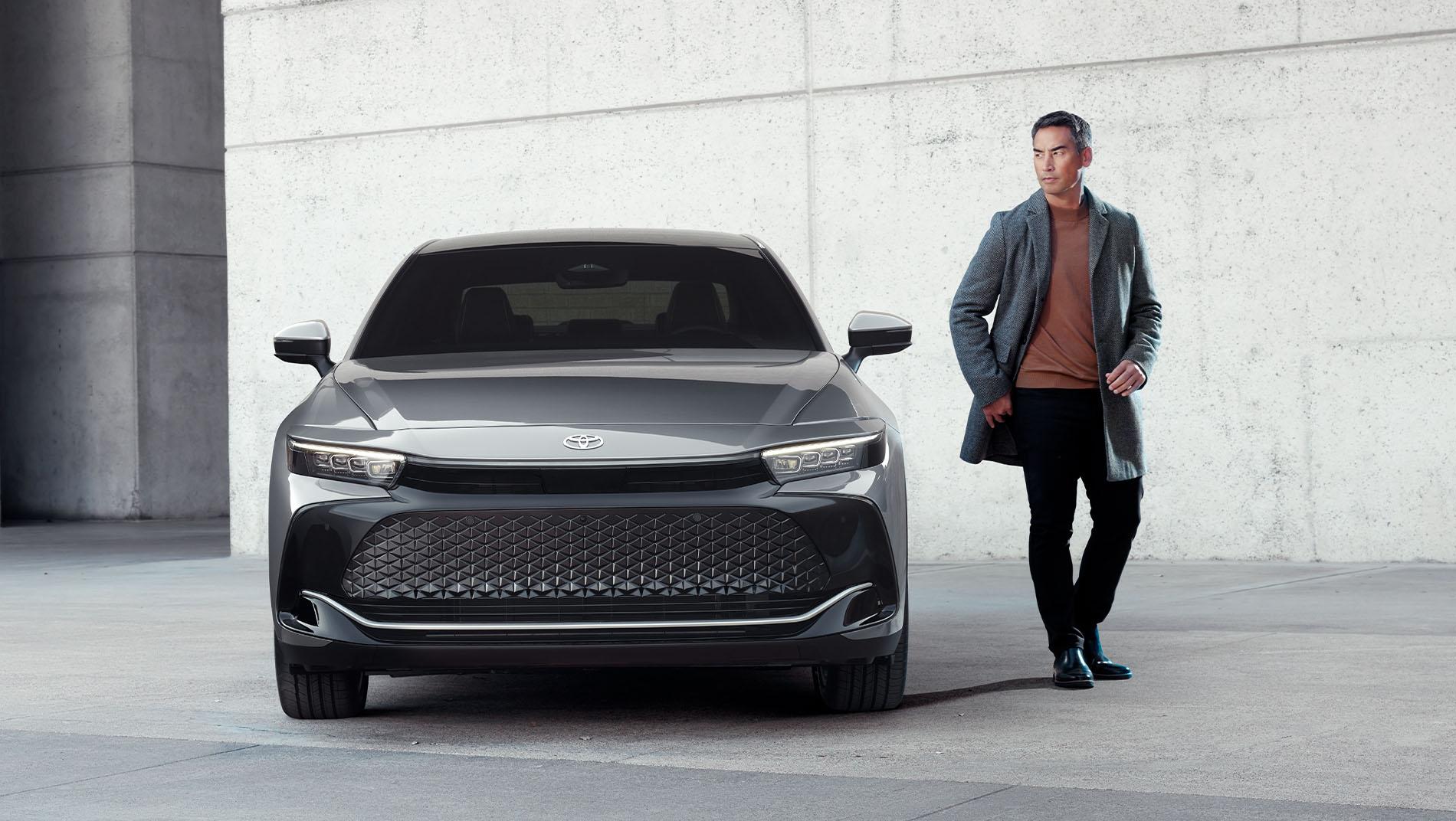 man standing beside a grey 2025 Toyota Crown with a concrete building behind them