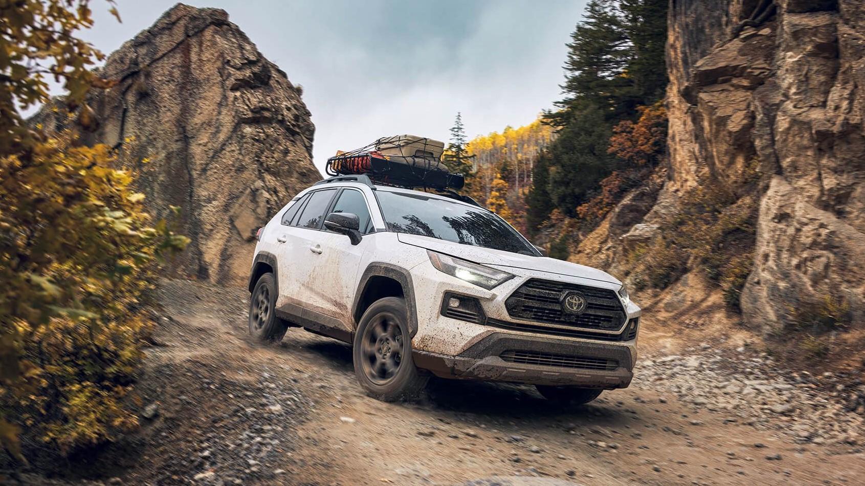 white 2024 Toyota RAV4 with roof rack full of gear going down a muddy mountain road