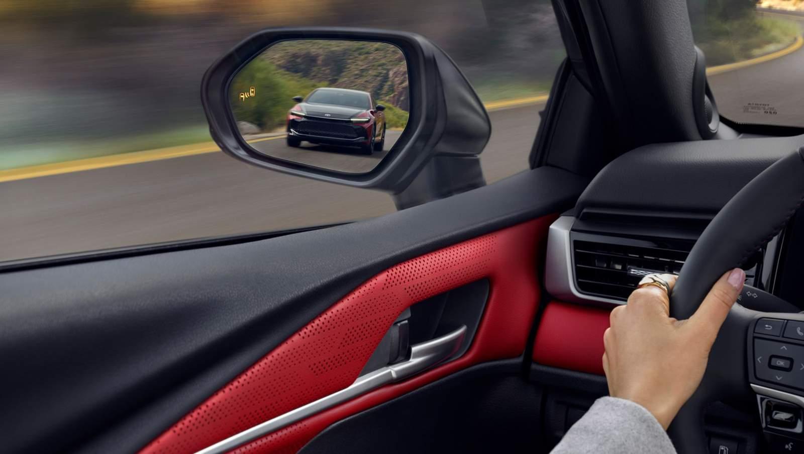 inside a 2 tone black and red Toyota Camry driving on a curved road with a sporty Toyota Camry showing in the side mirror