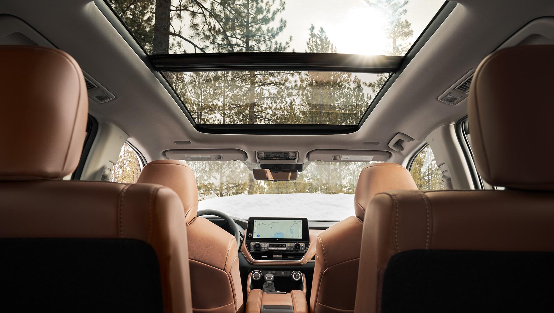 Inside a 2024 Toyota Grand Highlander shot from the third row looking through the brown leather 2nd row captains chairs and showing the panoramic sunroof