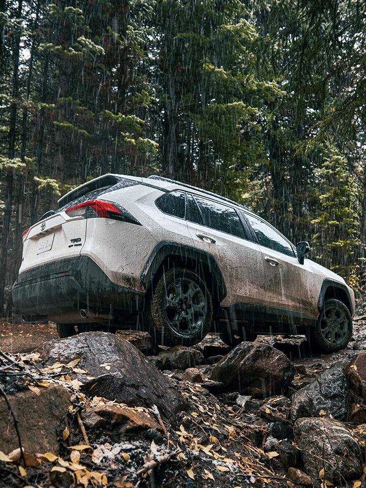 white Toyota RAV4 driving on a muddy mountain road in the rain