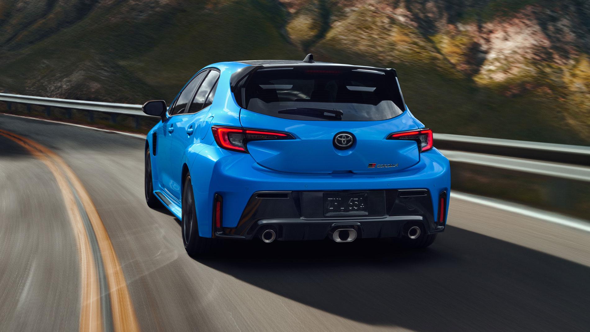 Blue 2024 Toyota GR Corolla driving on a highway next to a grassy mountain