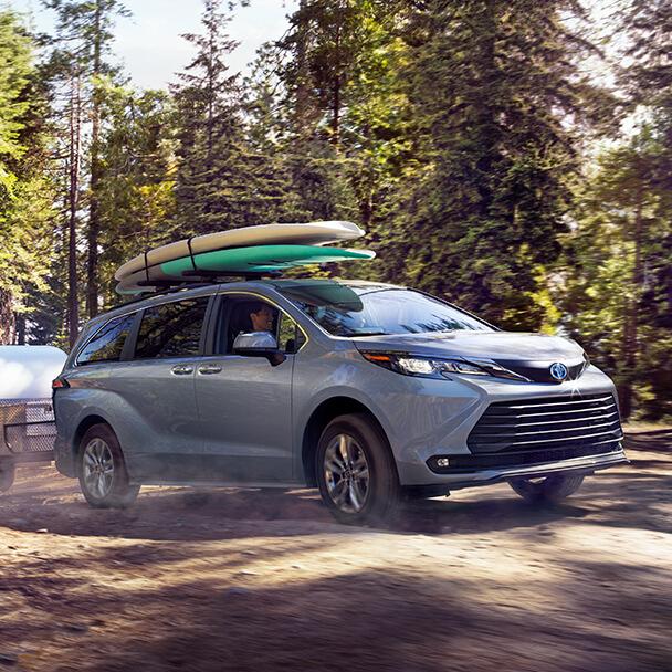 grey Toyota Sienna towing a camper with 2 paddle boards on top of the roof racks driving through the mountains
