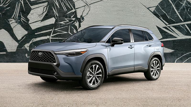 A silver SUV parked on a concrete surface in front of a mural featuring abstract black and white shapes and lines on a brick wall.