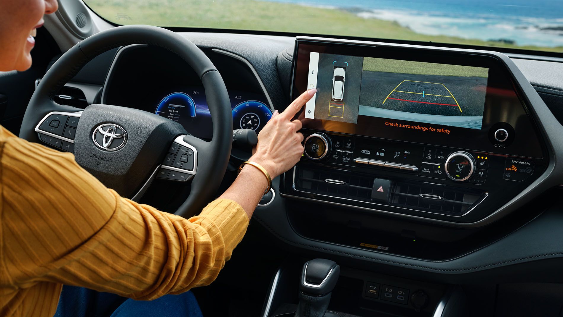 A person in a yellow shirt uses the touchscreen display of a Toyota car's dashboard, viewing the rearview camera parking assist