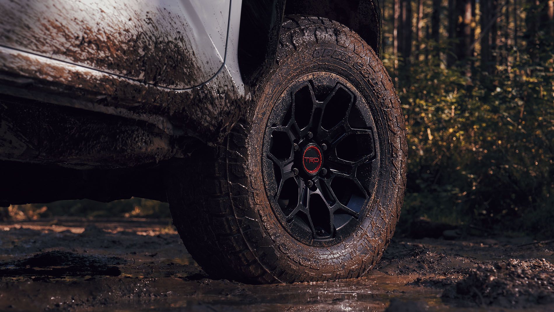 A close-up of a muddy off-road vehicle tire and wheel, partially covered in dirt, with a TRD logo on the hubcap.