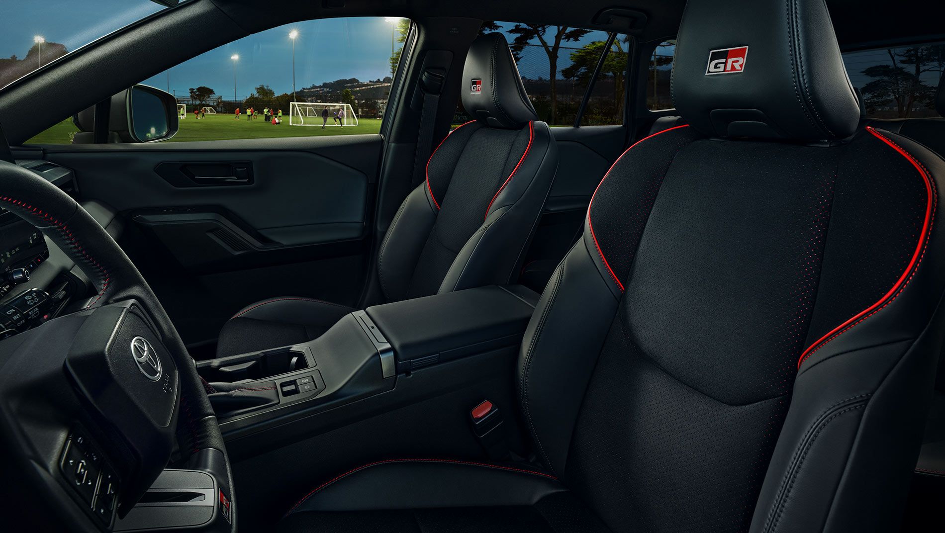 Interior of a modern car showing black front seats with red stitching and a “GR” logo, dashboard, steering wheel with Toyota emblem