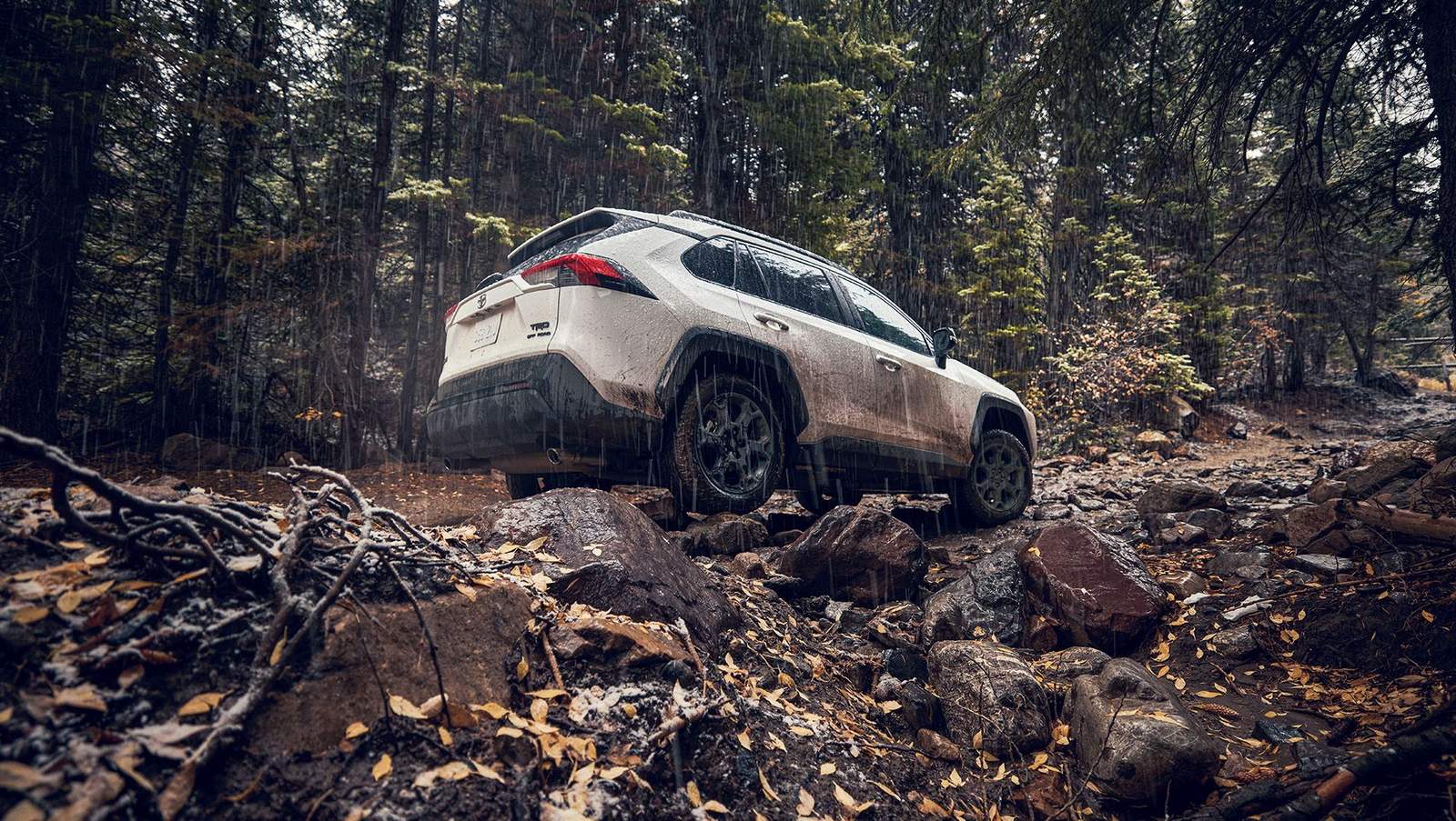 white Toyota RAV4 driving through a mud train in the mountains while it's raining
