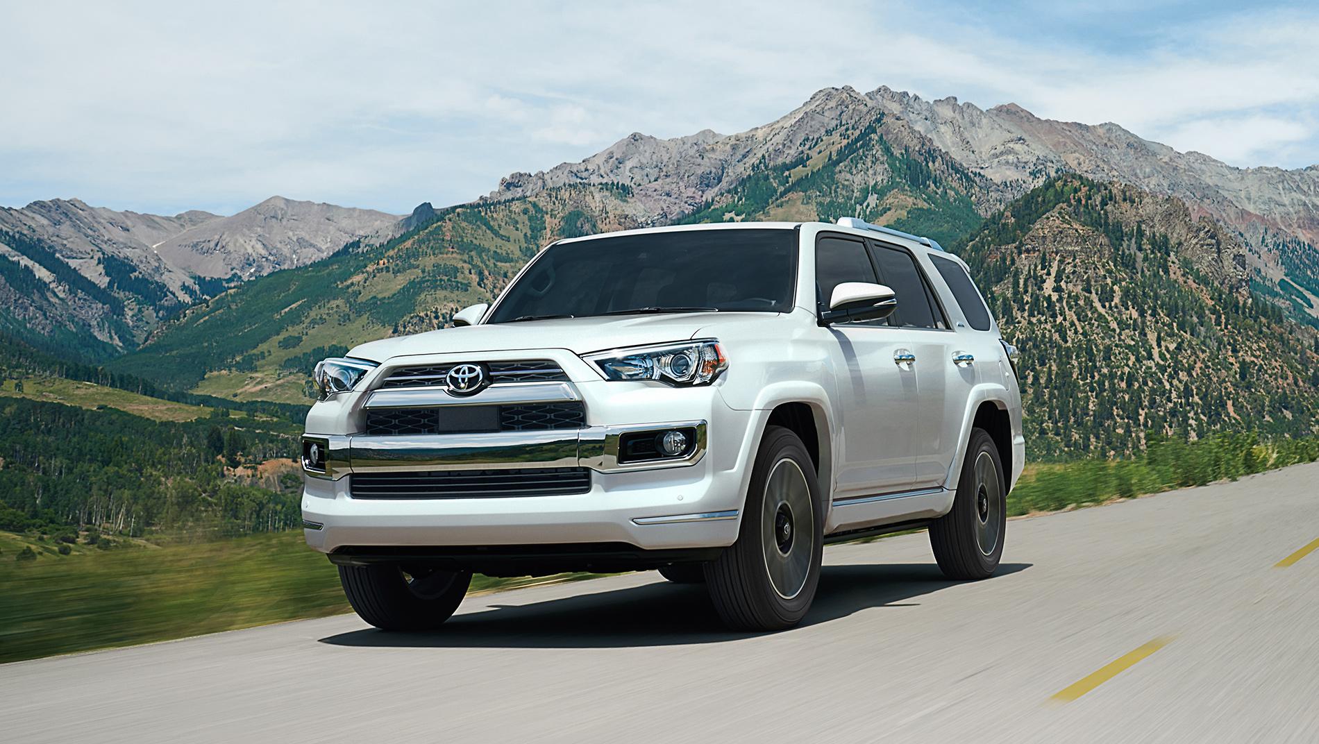 White 2024 Toyota 4Runner driving down a road with rocky mountains beyond