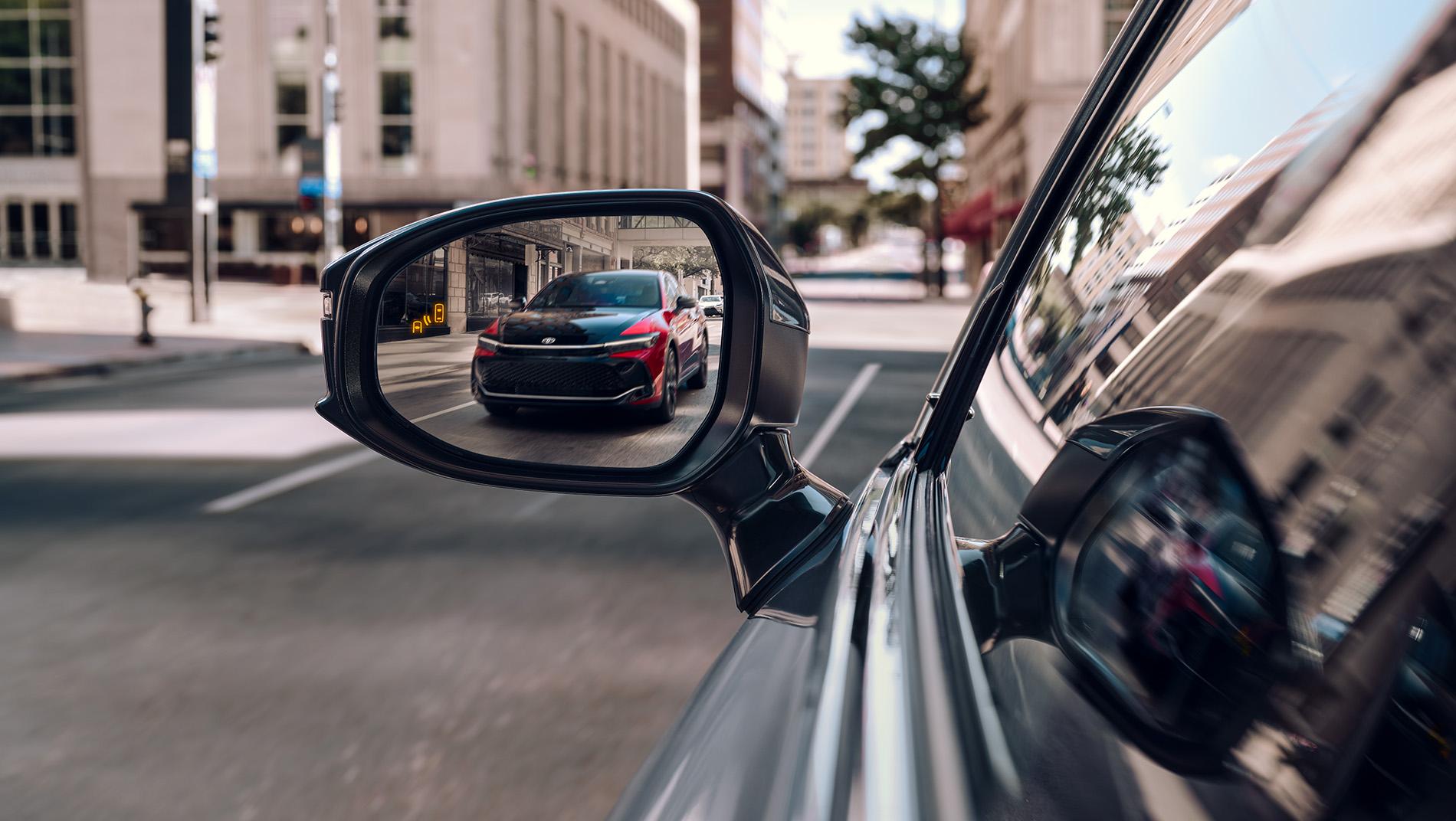 2 toned red 2025 Toyota Crown hybrid being shown in the side mirror of another Toyota Crown as they drive down a city street