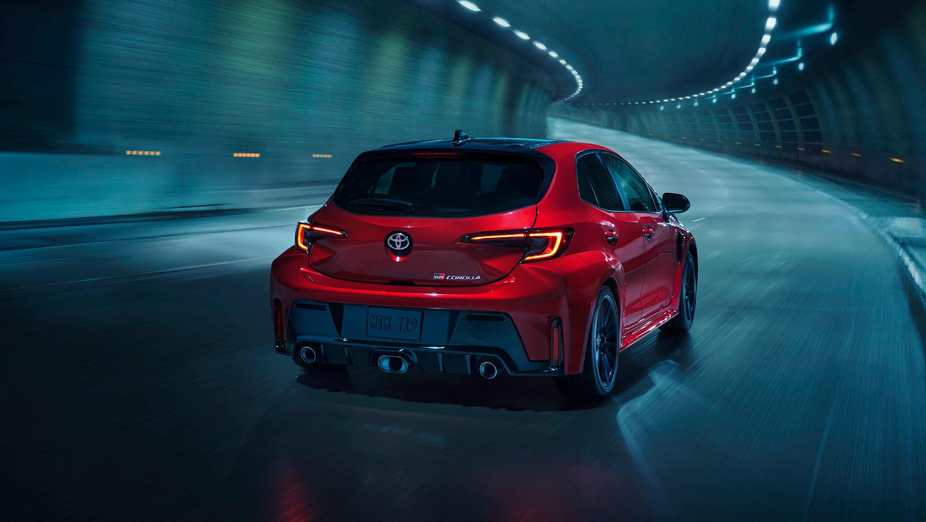 A red 2025 toyota gr corolla drives through a dimly lit tunnel.