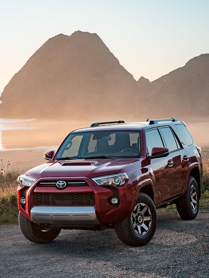 Red Toyota 4Runner SUV parked in front of beach in front of mountains