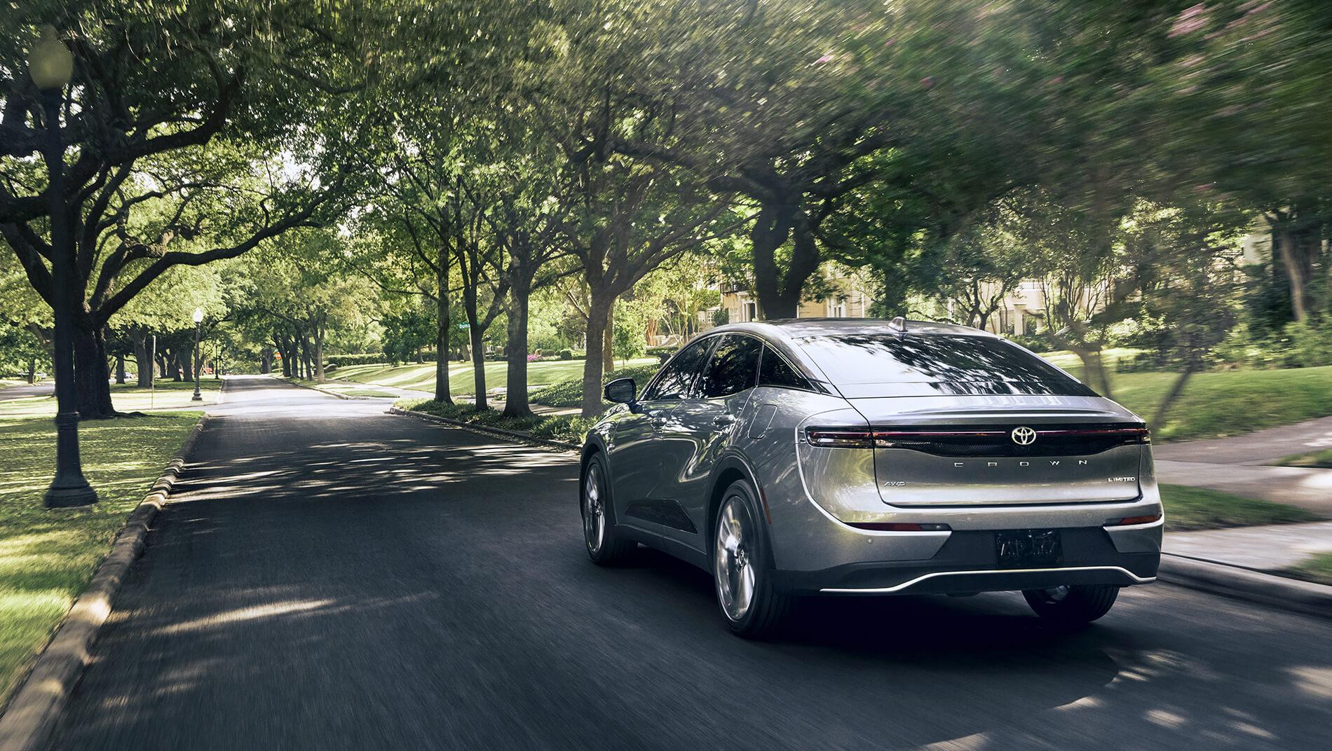silver 2023 Toyota Crown driving through a green park with lush trees