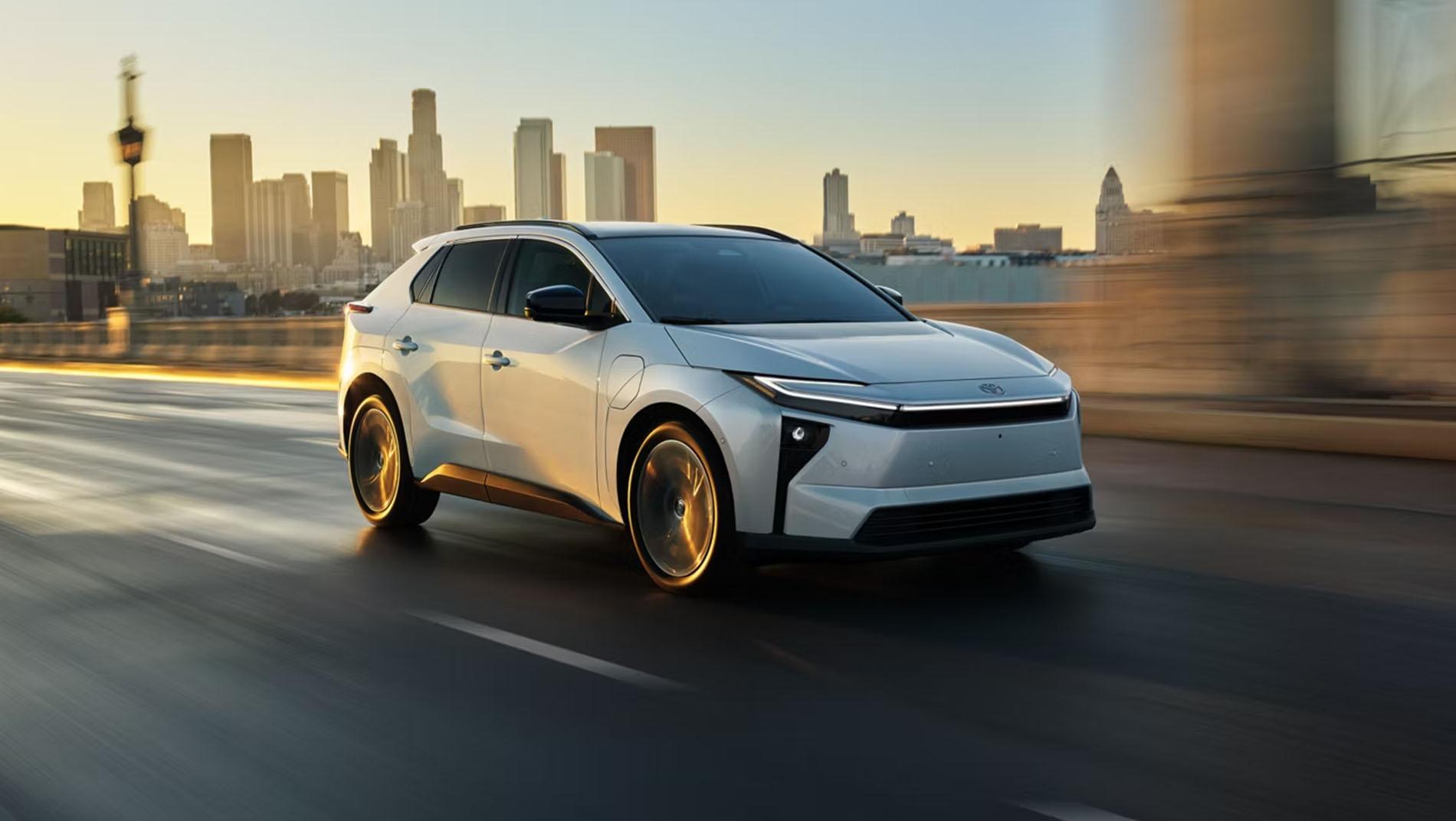 A sleek white toyota electric SUV drives on a city street at sunset, with a blurred background