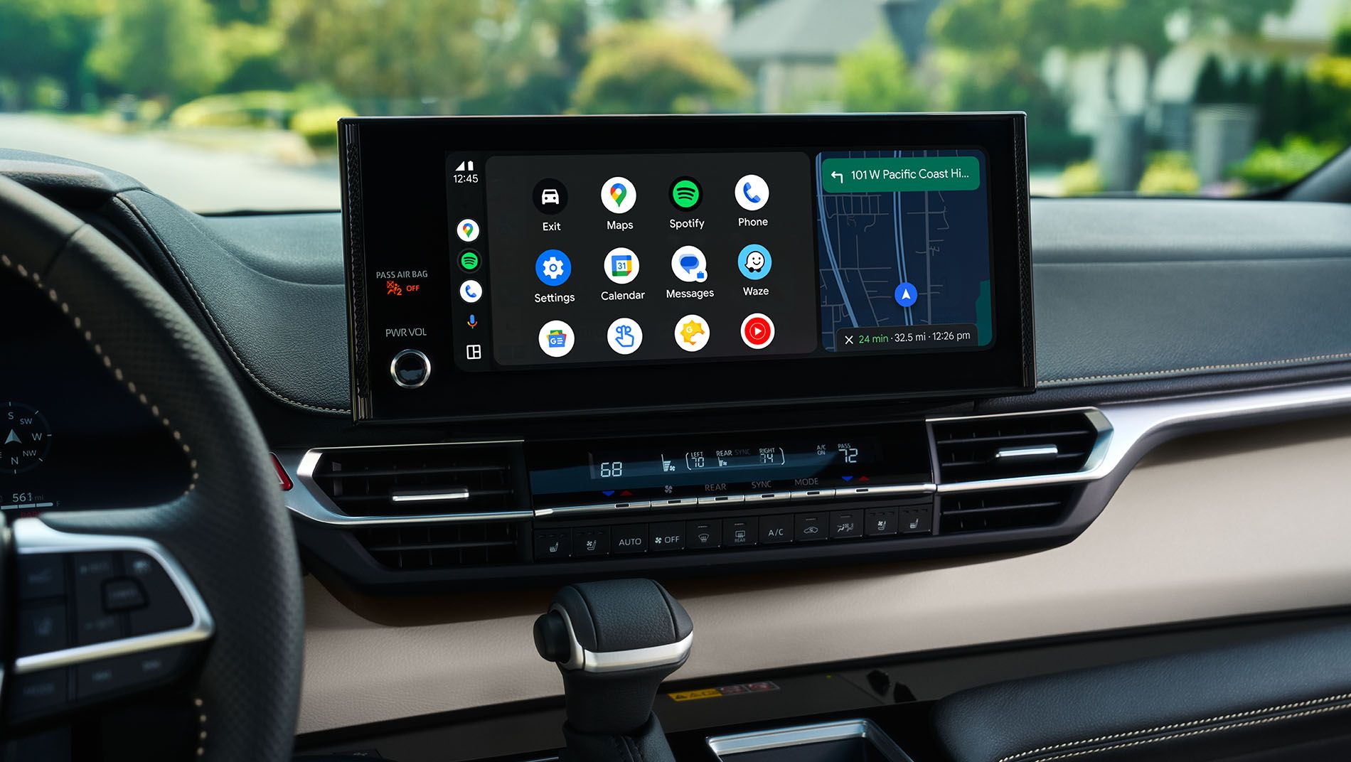 A car’s dashboard displays a large touchscreen with Android Auto interface, showing app icons and a navigation map. The gear shift and part of the steering wheel are also visible inside the modern vehicle.