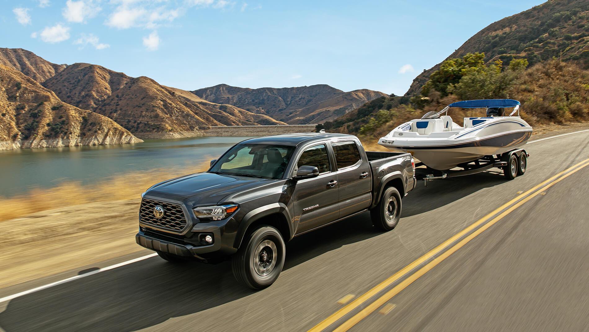 grey Toyota Tacoma towing a boat past a lake in the mountains