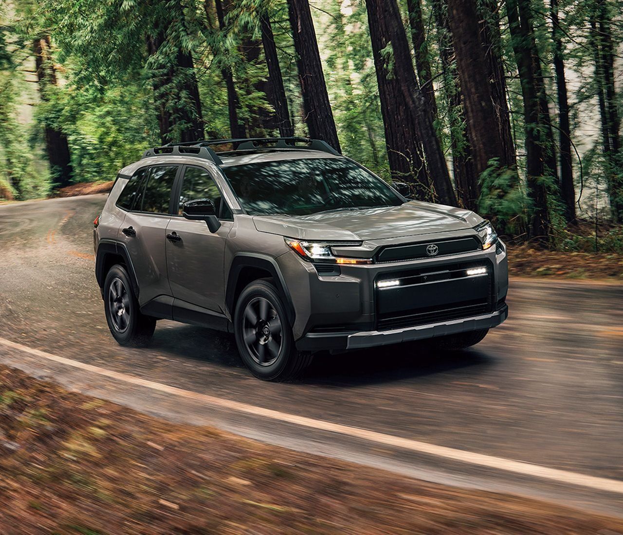 A gray Toyota rav4 SUV is driving on a street lined with and trees.