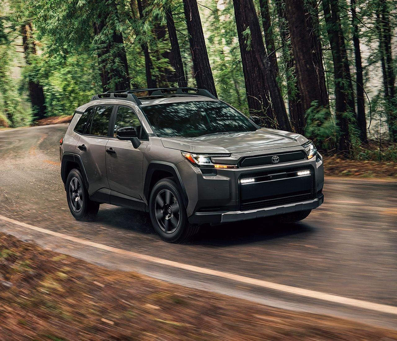 A gray Toyota rav4 SUV is driving on a street lined with and trees.