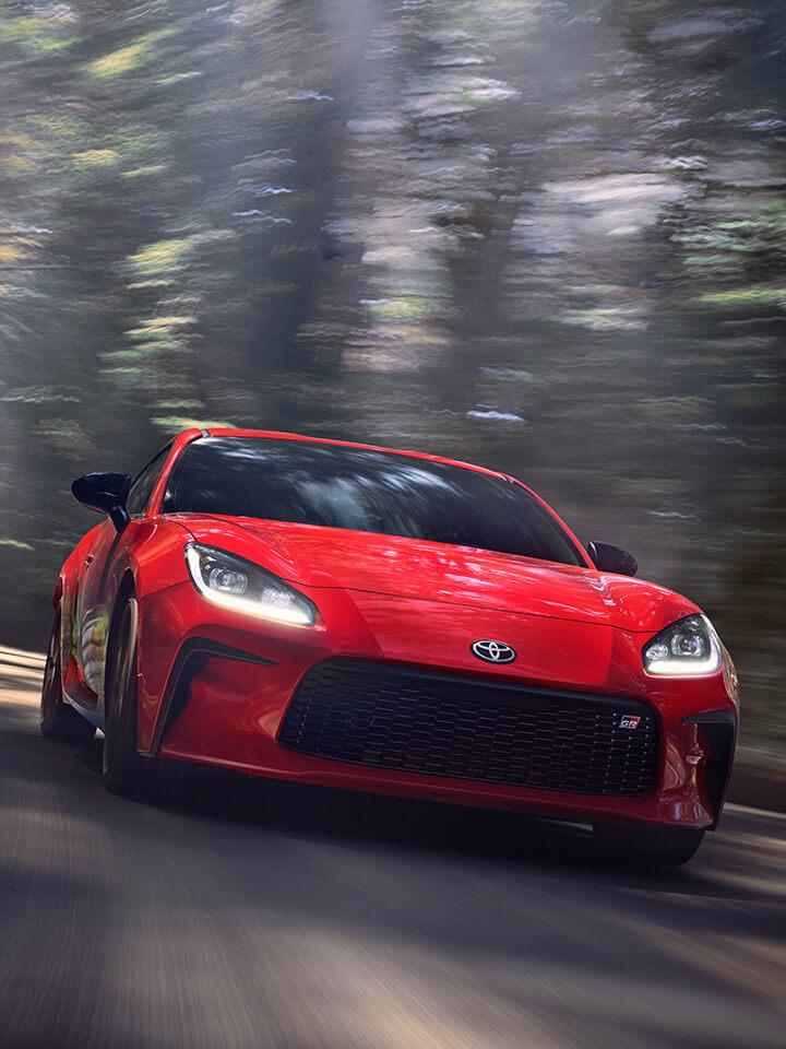 Red Toyota Sedan driving down a forest road