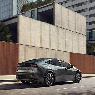 exterior image of a Grey 2024 Toyota Prius Prime plug in hybrid driving down a city street