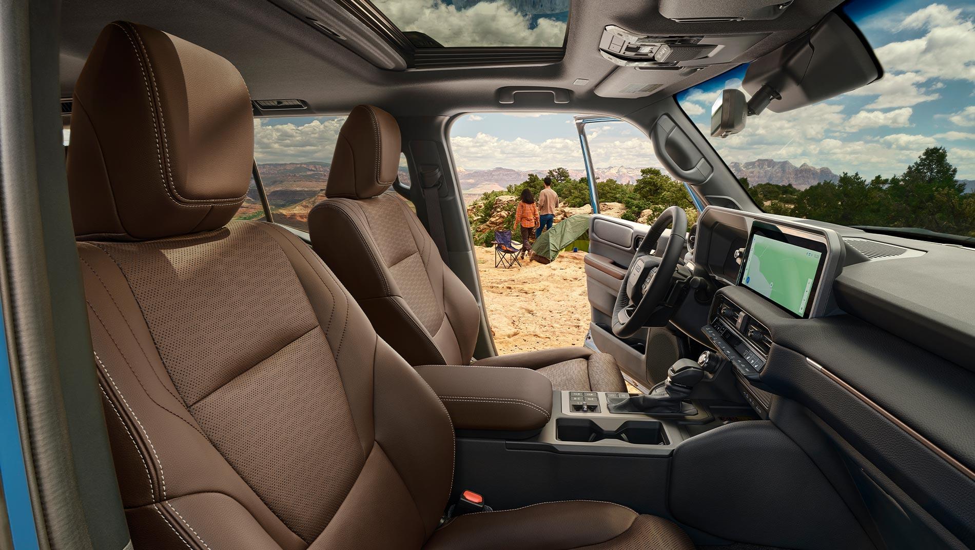 inside the front of the 2025 Toyota Land Cruiser hybrid with the sunroof and navigation system. the drivers door is open showing 2 people setting up camp on a mountain top