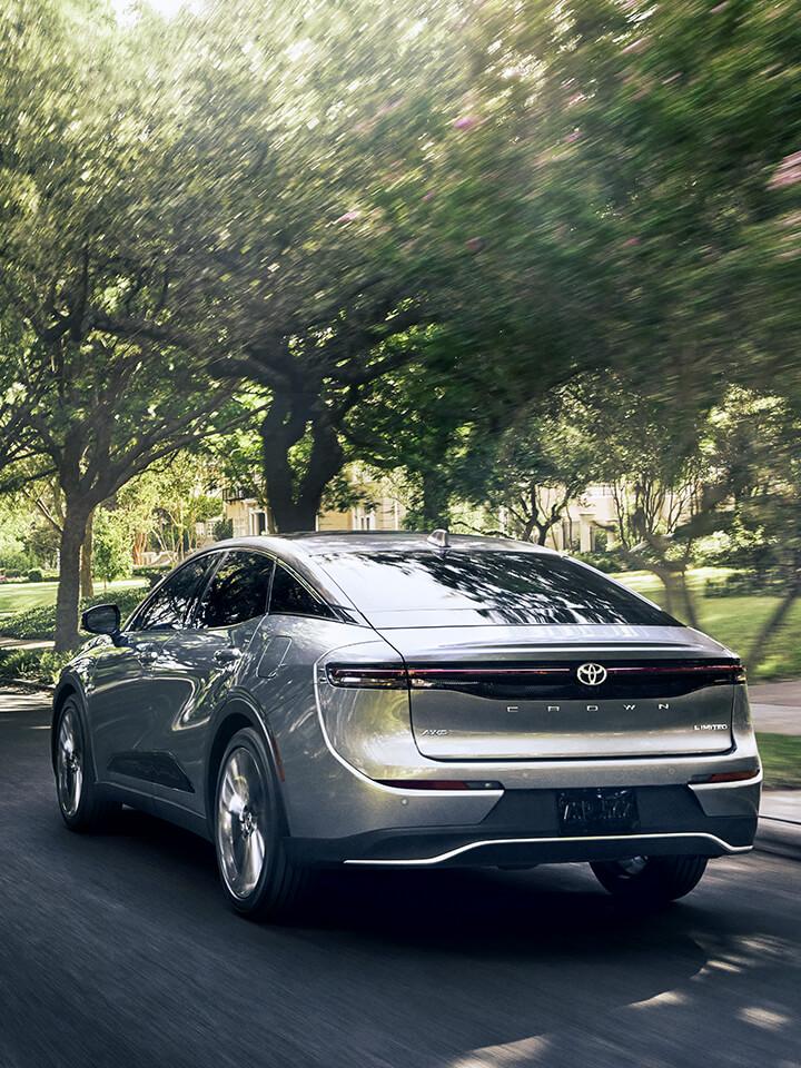 silver Toyota 2023 Crown driving next to a green park with trees