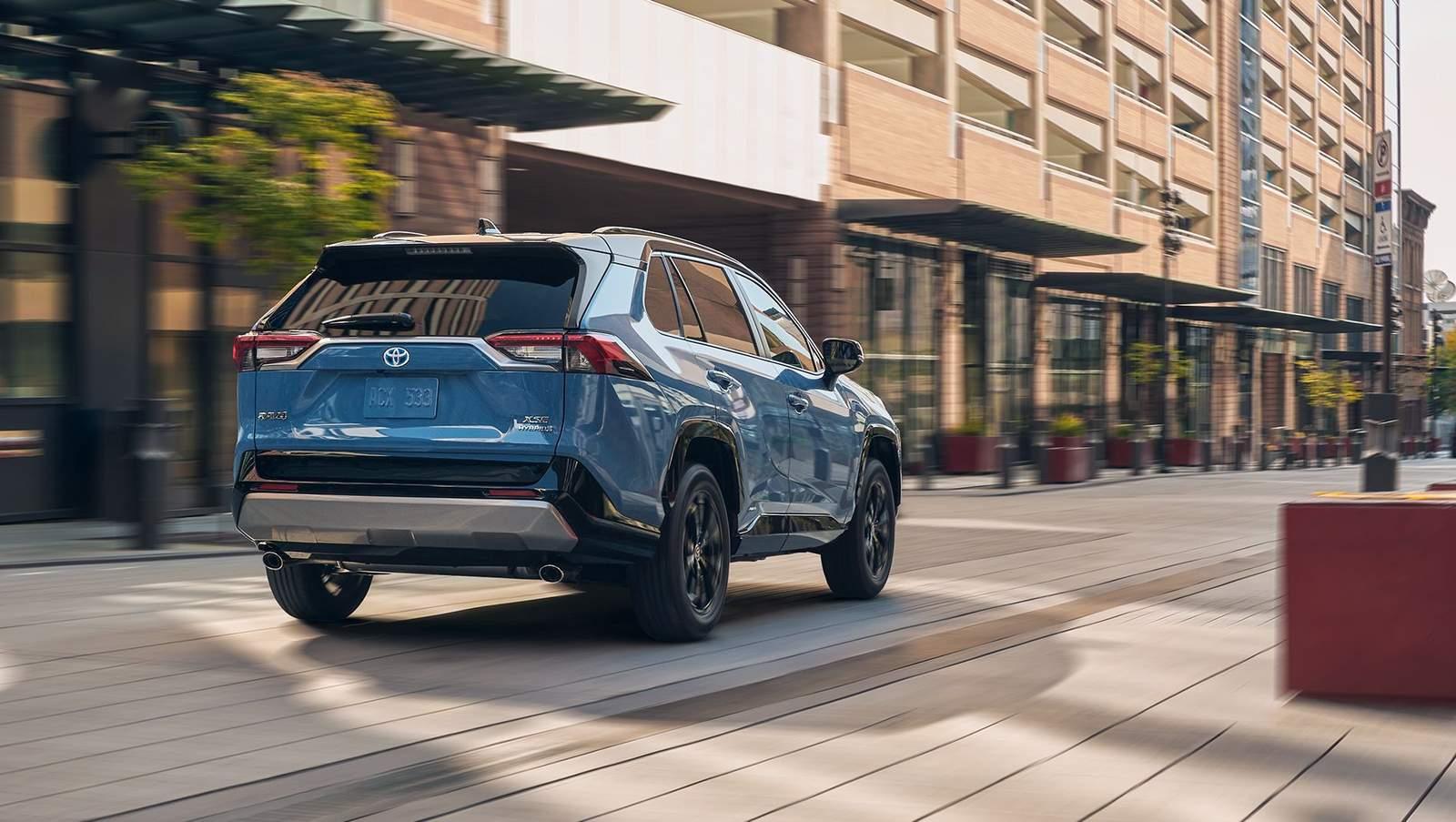 blue 2024 Toyota RAV4 shot from behind driving down a shopping center alley