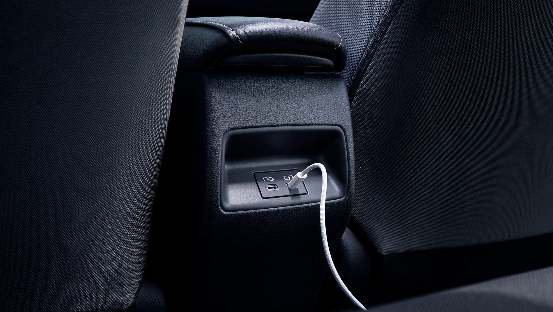 A close-up view of a car’s rear seat center console featuring USB charging ports, with a white charging cable plugged into one of the ports.