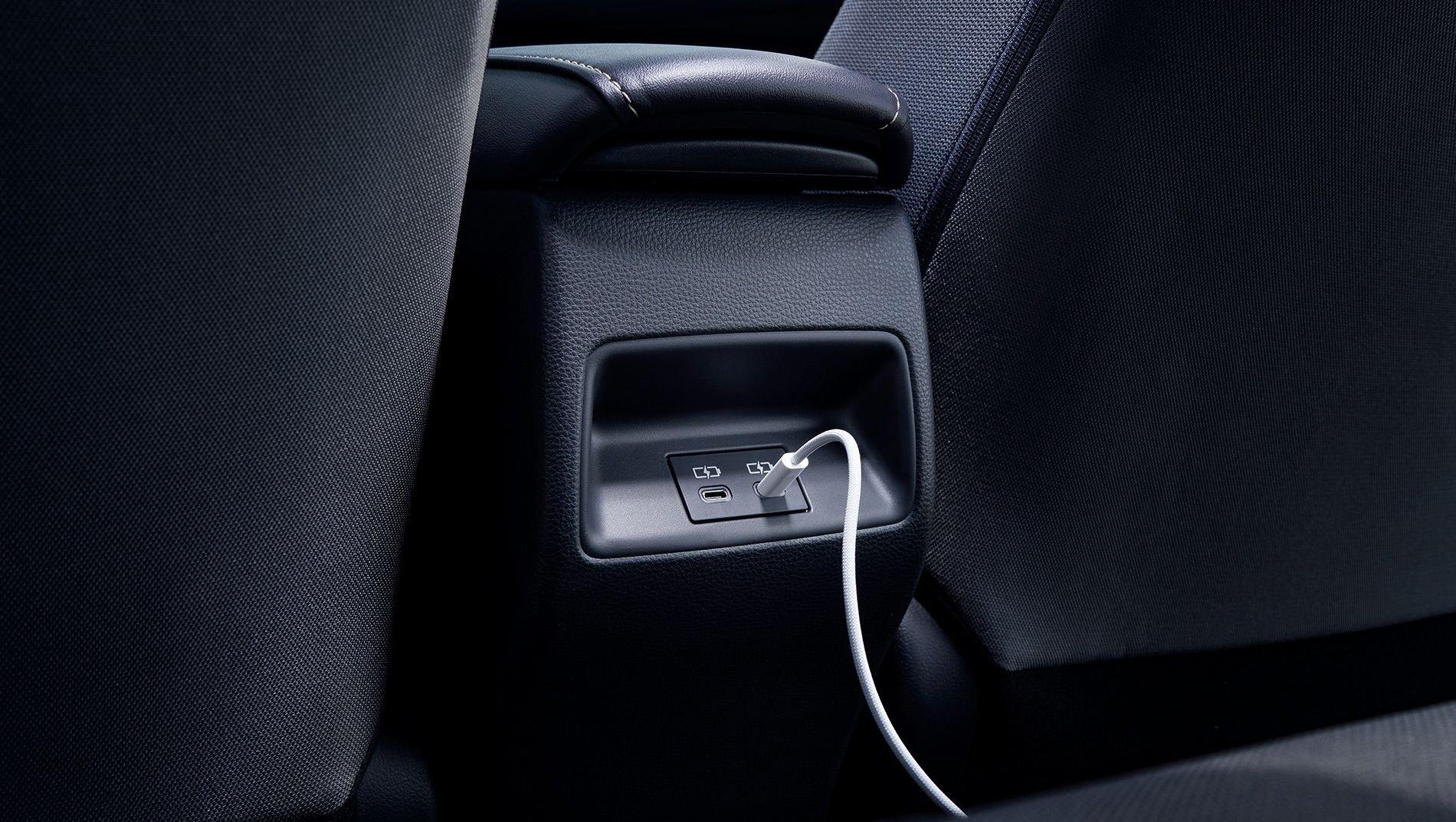A close-up view of a car’s rear seat center console featuring USB charging ports, with a white charging cable plugged into one of the ports.