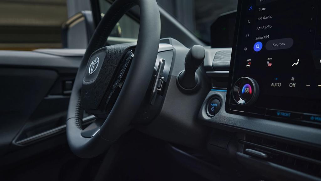Close-up of a Toyota car interior showing the steering wheel, dashboard controls, and a large touchscreen display with climate and audio settings visible.