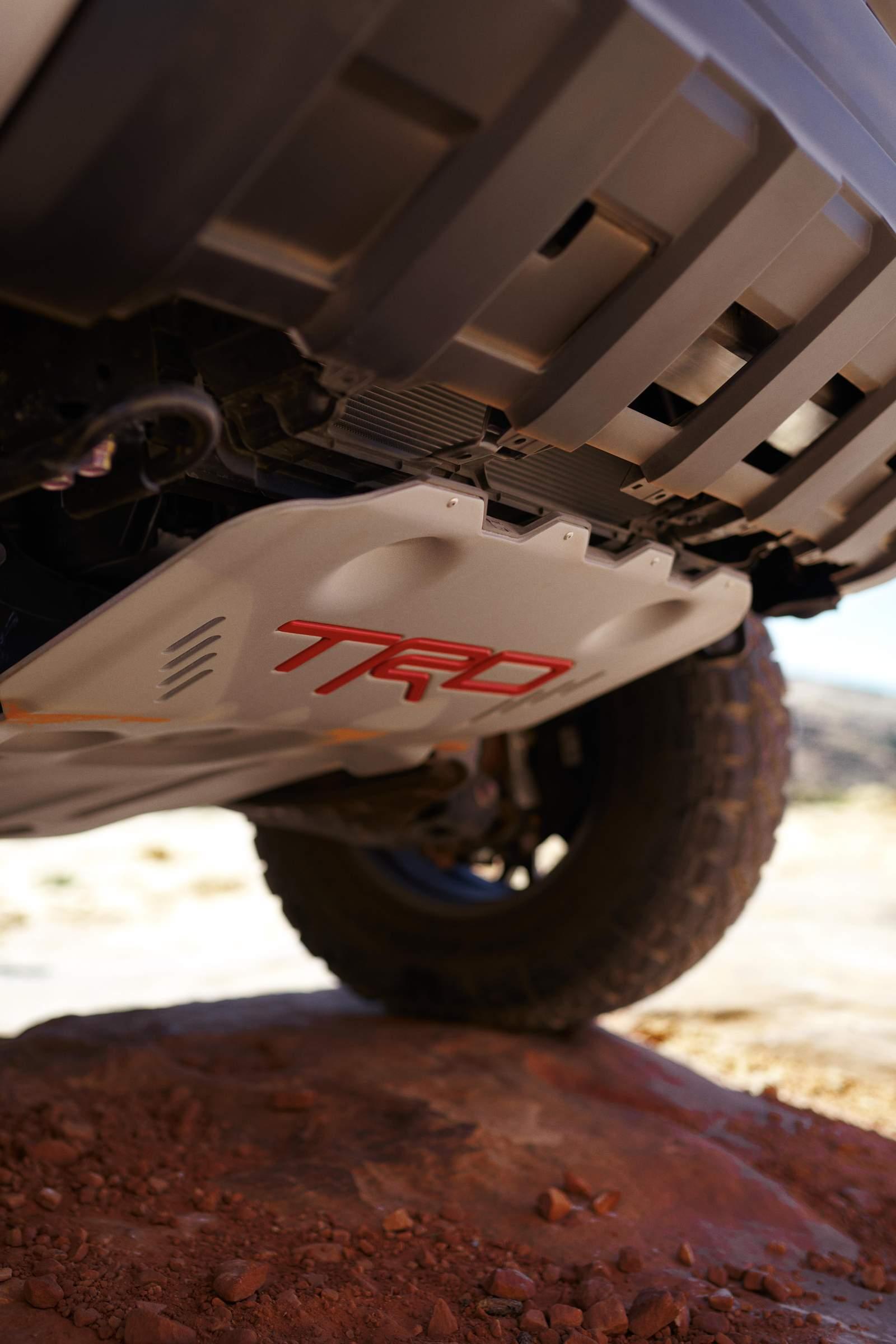 Low-angle view of a rugged toyota tacoma undercarriage with a TRD skid plate, partially on a rocky terrain.