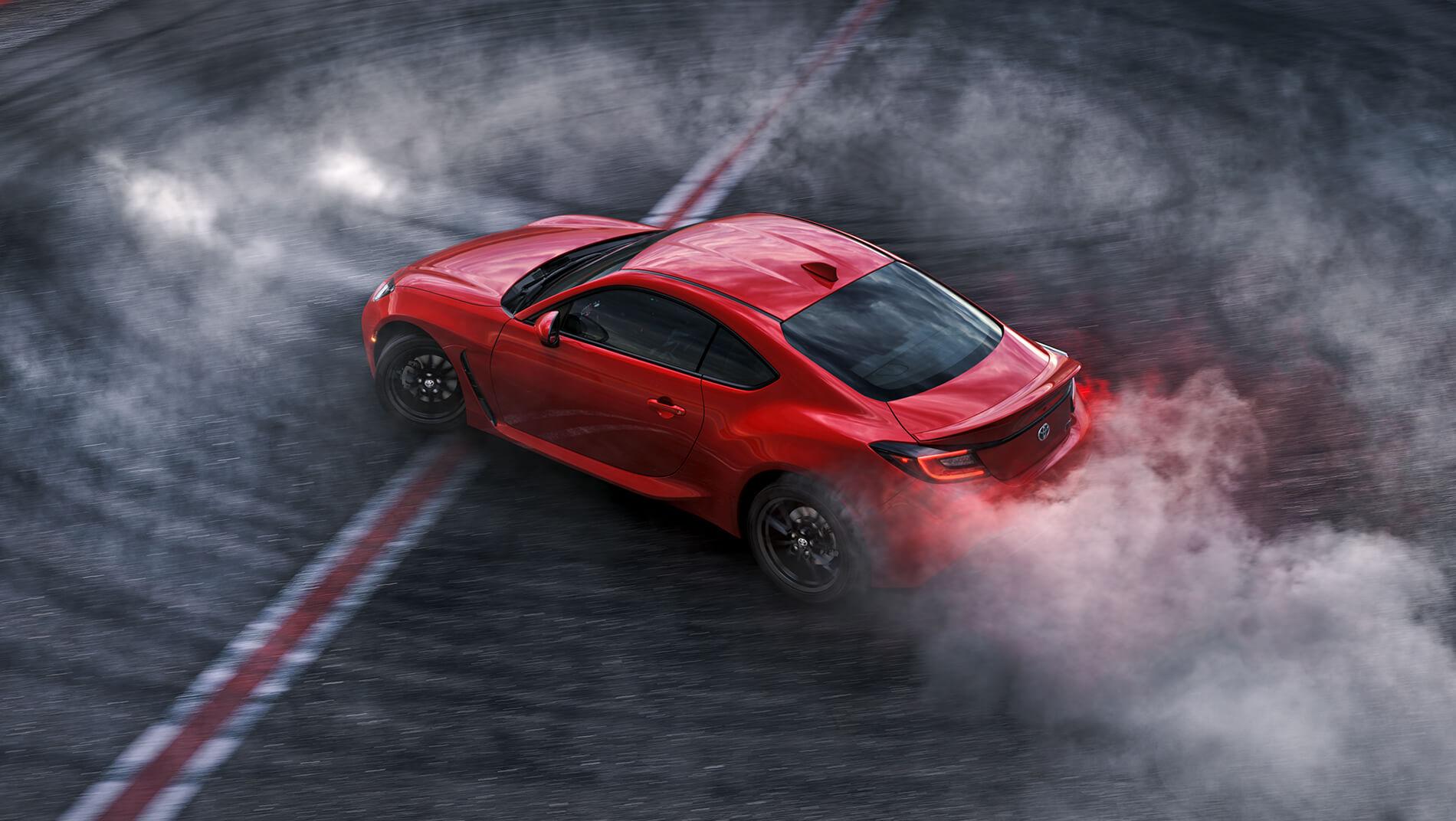 red 2023 Toyota GR86 with smoke coming from the tires as it races around a race track