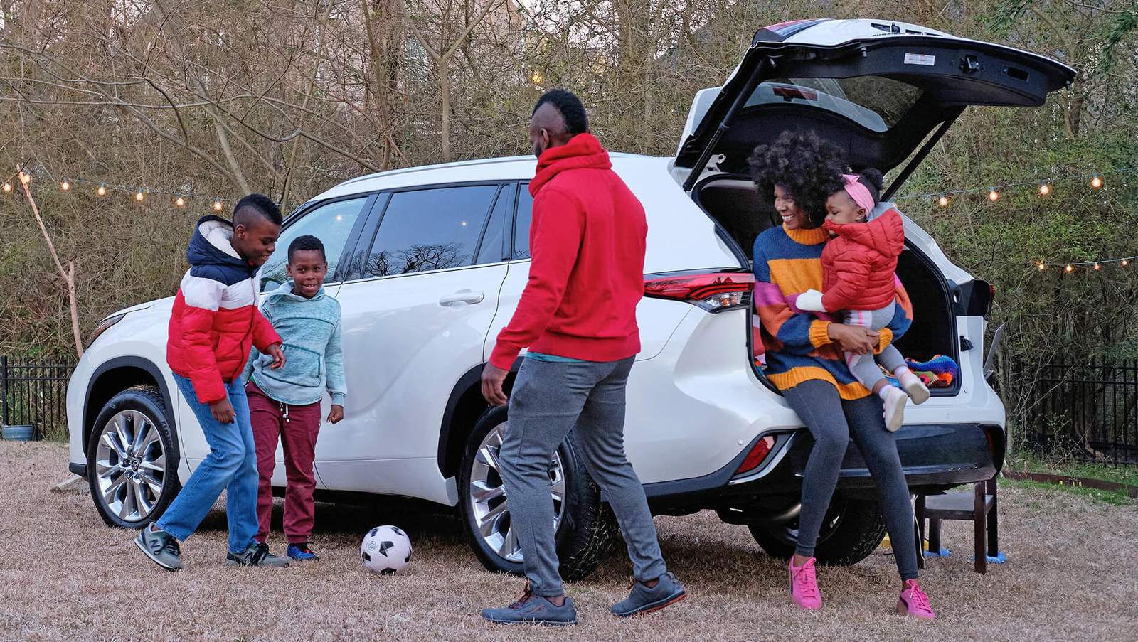 Family plays with soccer ball in front of white Toyota Highlander