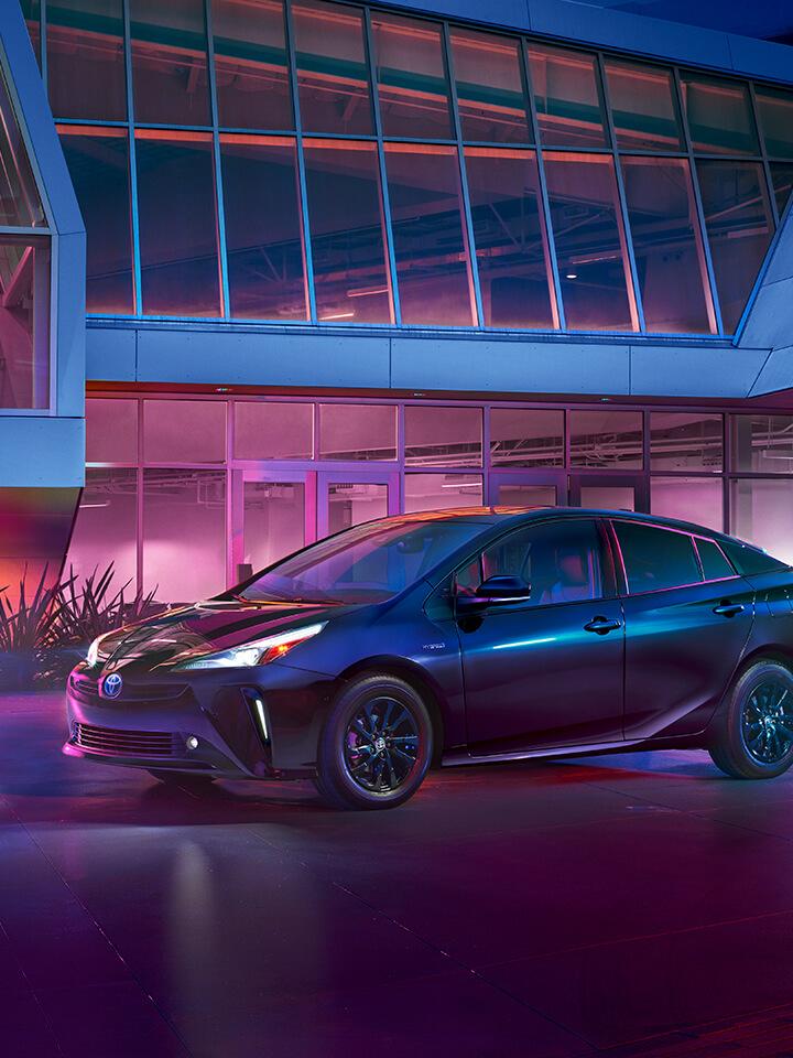 black Toyota Prius parked in front of a modern building at night with purple lighting