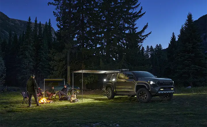 New Toyota Truck with camping accessories set up in field with people around a campfire