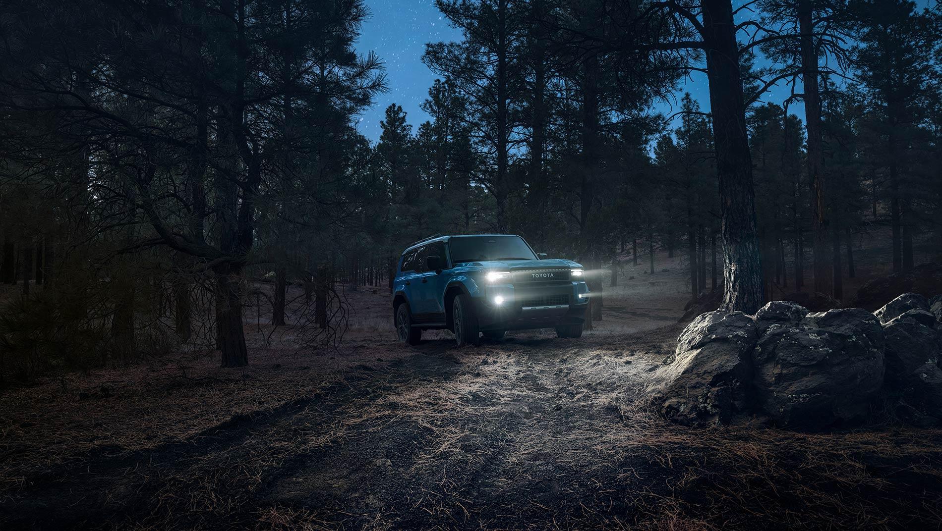 blue 2025 Toyota Land Cruiser driving down a mountain road at night