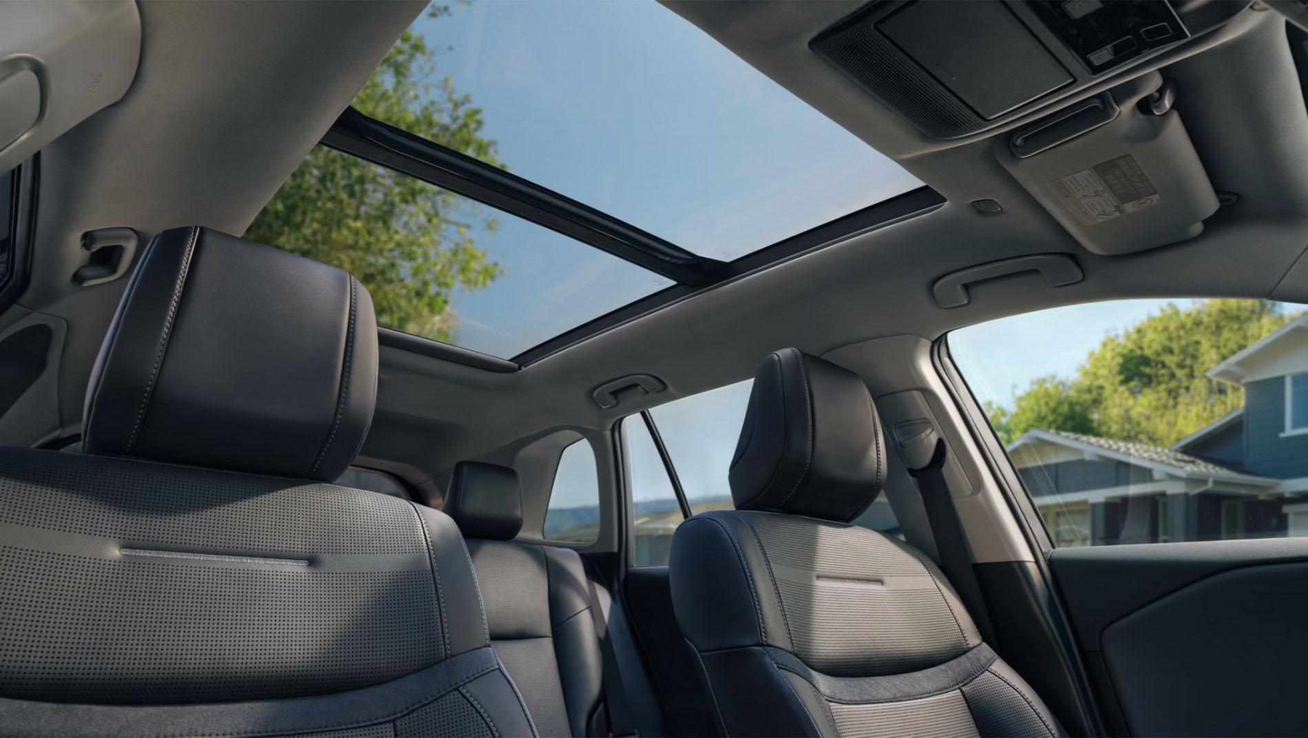 View of a car’s front seats and interior, featuring a panoramic sunroof with blue sky and trees visible through the glass
