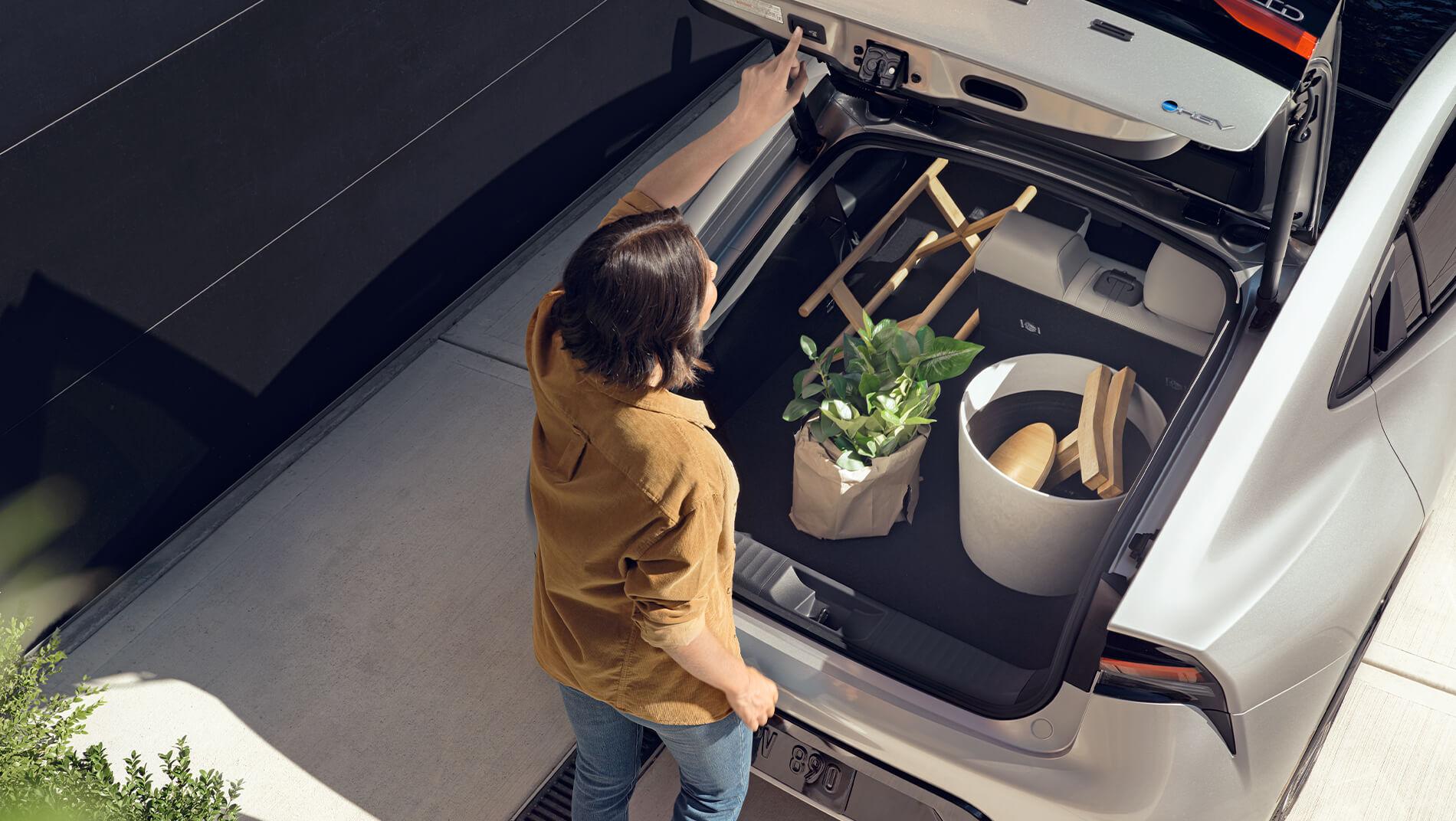 Woman loading cargo into the cargo area of a Prius and closing the door with 1 touch button power lift gate