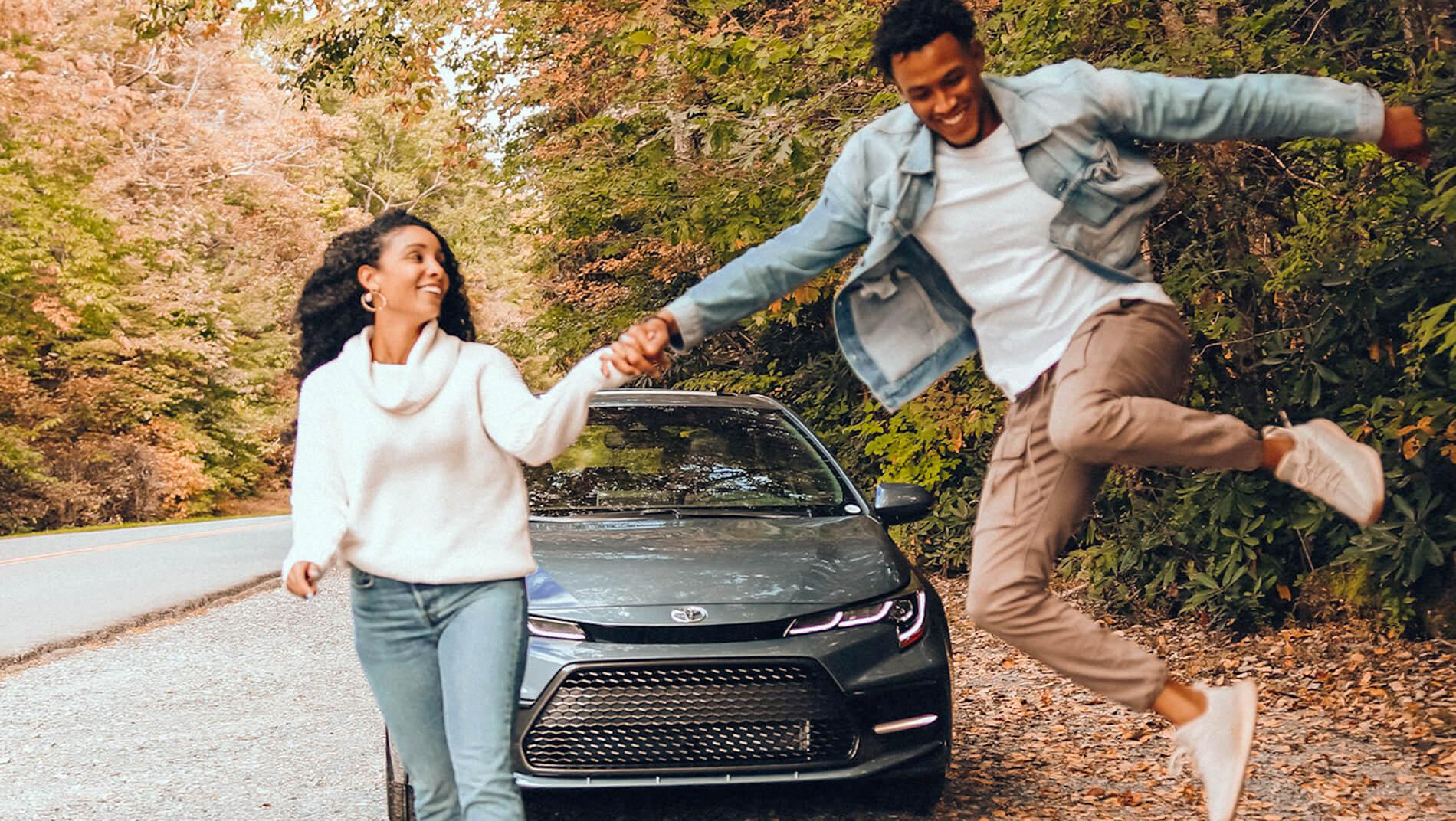 woman holding mans hand as he jumps happily in front of Toyota Corolla